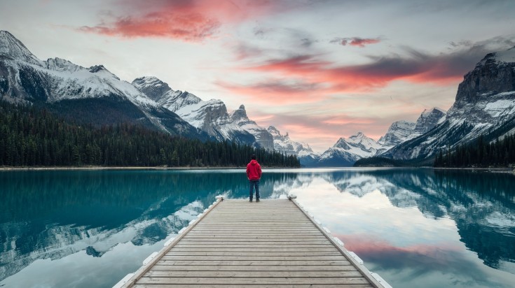 A man on a pier at sunset in Maligne Lake, Canada in November.