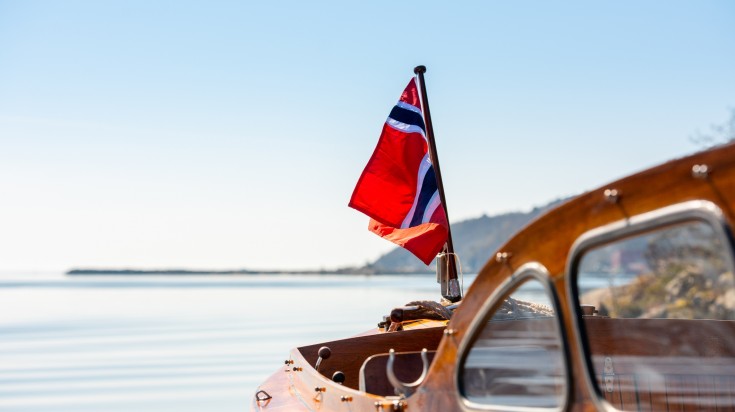 The norwegian flag in the aft mast of a wooden boat.