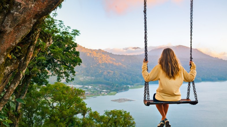 A girl sitting on a tree rope swing on high cliff and enjoying the view of Bali Island in Indonesia in November.
