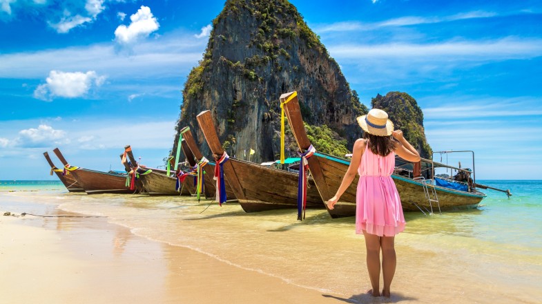 A tourist woman near a traditional longtail boat in Phra Nang Beach during summer in Thailand.