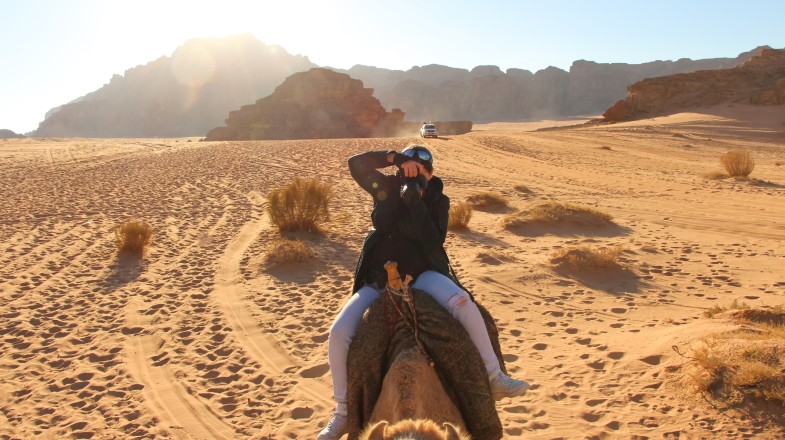 A woman rides a camel through the Wadi Rum desert during her Jordan adventure tours.