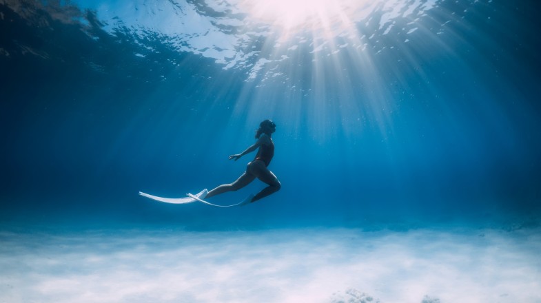 Freediver with white fins glides and posing underwater in ocean in Mexico in April.