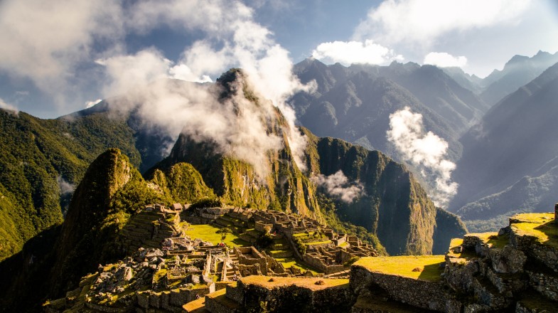 The ancient ruins of Machu Picchu in the Peruvian Andes with clouds and hills in the distance.