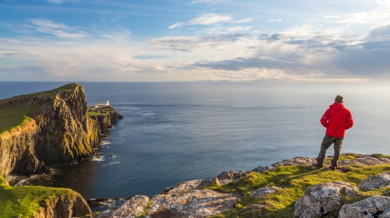 A man admiring the view of lighthouse in Isle of Skye which is one of the best places to visit in Scotland.
