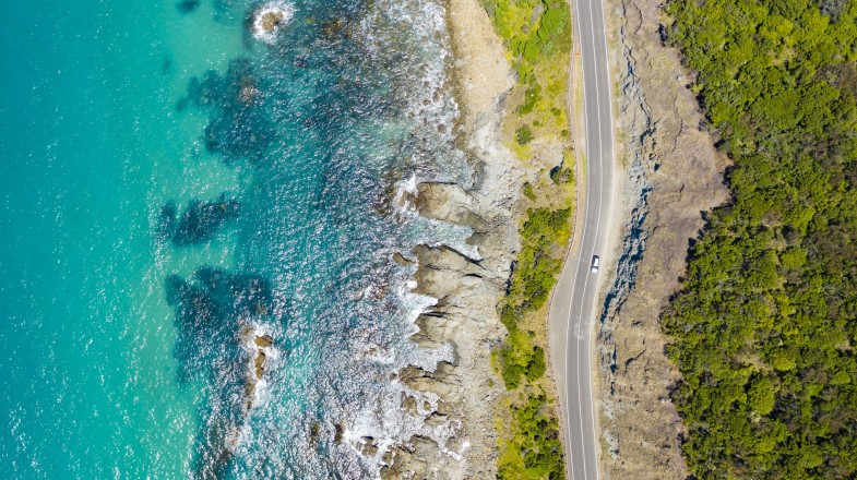 An aerial view of a section of Great Ocean Road with the turquoise waters on one side and the green forest on another.