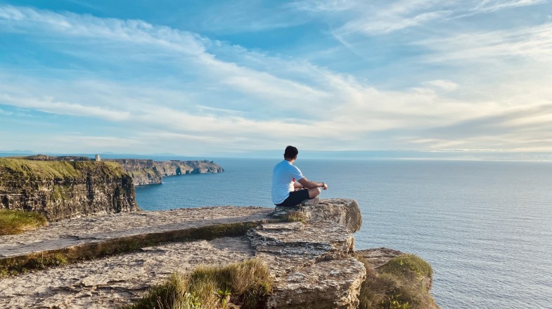 A traveler sitting at the edge of Cliffs of Moher admiring the view, one of the top 10 things to do in Ireland.