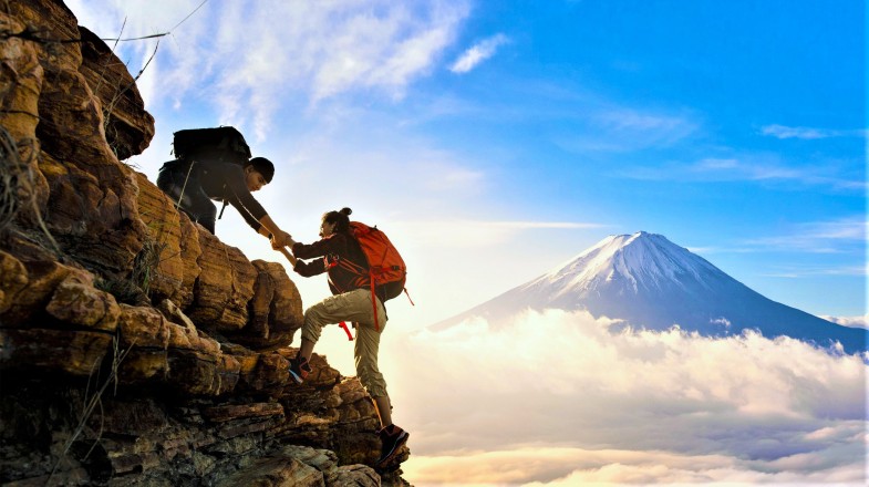 A hiker helps his friend climb up the hill during their travel.