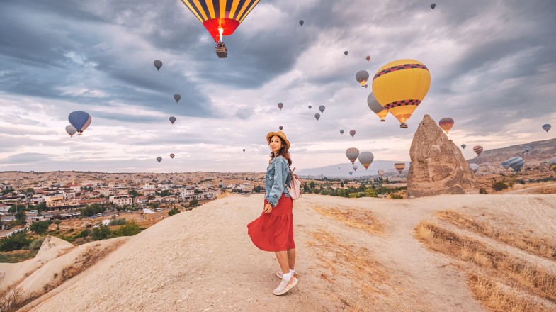 A girl in a red dress at Cappadocia with hot air balloons in the sky during Turkey walking tours.