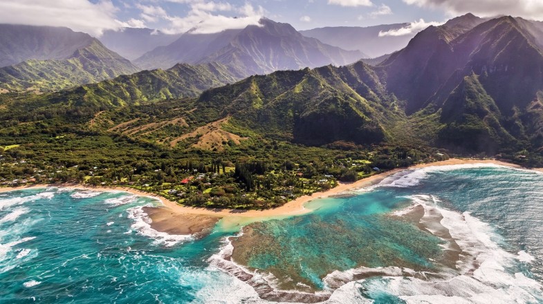 Miles of beach lined by turquoise sea water and mountains in the background.